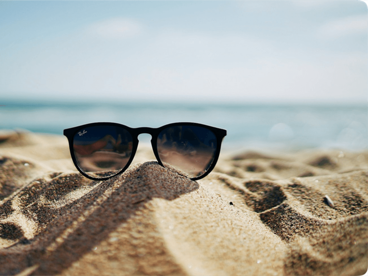 Solbriller står på en sanddyne med havet i bakgrunnen, som gir en sommerlig stemning.