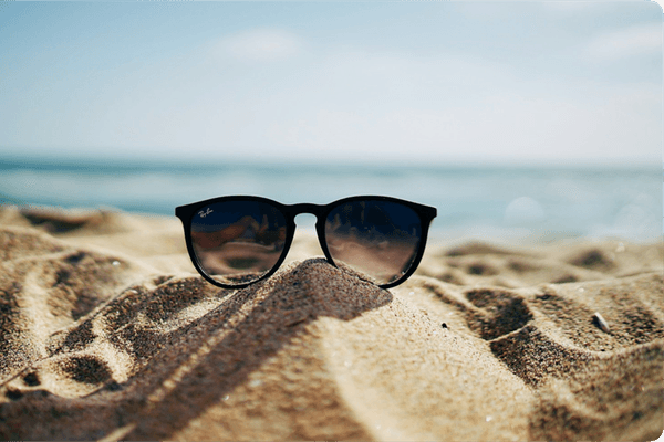 Solbriller står på en sanddyne med havet i bakgrunnen, som gir en sommerlig stemning.