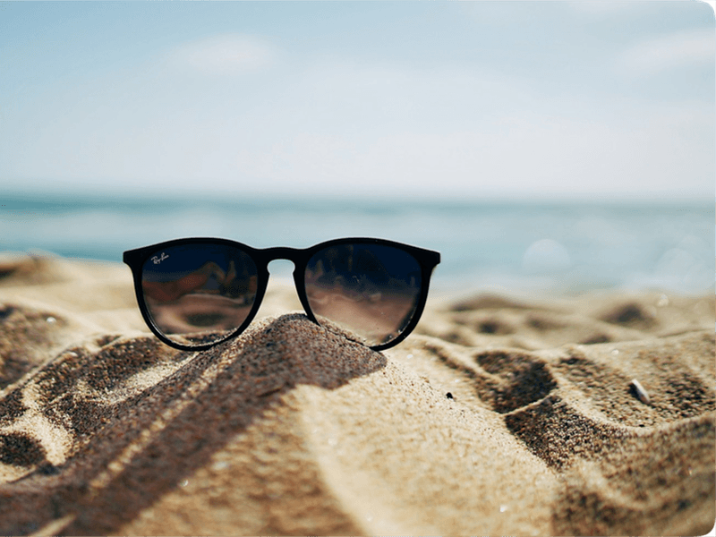 Solbriller står på en sanddyne med havet i bakgrunnen, som gir en sommerlig stemning.